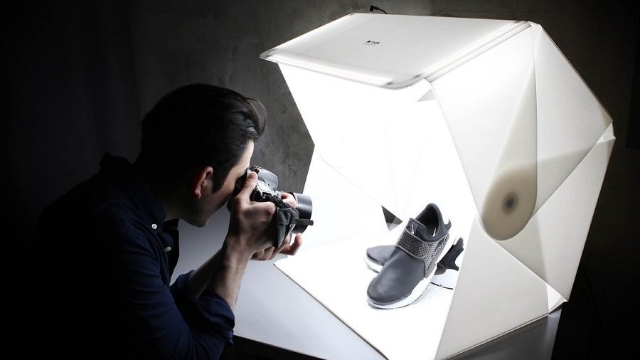 A picture of a man capturing a photo of a pair of shoes placed inside a light box